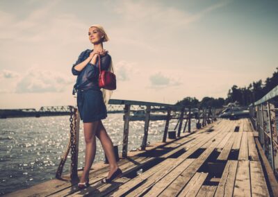Élégant belle femme blonde avec écharpe blanche et rouge sac debout près des rails de vieux quai