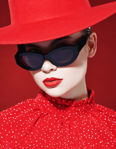 Photo de mode d'une jeune femme élégante au maquillage éclatant, vêtue d'une robe rouge, d'un chapeau rouge et de lunettes de soleil. Fond rouge. Beauté, maquillage et cosmétiques.